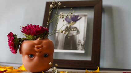 A flower bouquet inside an upside mannequin baby head in front of an old photograph of a ladya