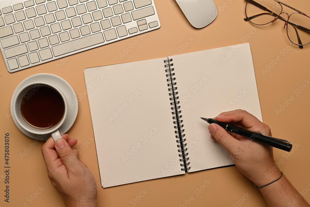 Poster top view image of hand taking notes and holding a coffee cup at the working desk surrounded by a key