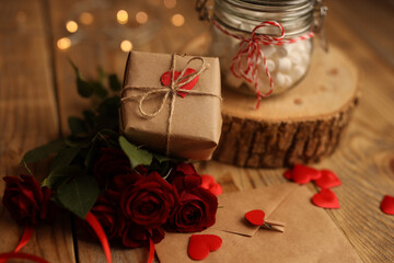 A gift in craft paper on a wooden background, red roses around, a jar of marshmallows, a letter in...