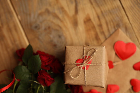 A gift in craft paper on a wooden background, around red roses and hearts. Picture for Valentine's Day. The concept of gifts and lovers. High-quality photography