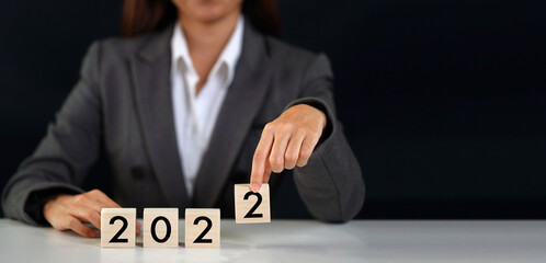 Businesswoman hand holding wooden cube block with number 2022 on table, new year calendar concept