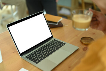 Close-up image of a freelance man holding a coffee cup at the wooden working desk surrounded with a white blank screen computer laptop and personal equipment.