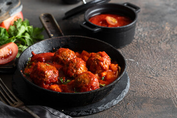 .Tender and fluffy meatballs with tomato sauce into flying pan on he cocnrete table with vegerables ingridients.
