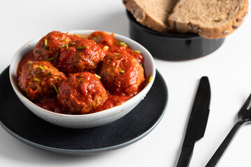 .Baked Meatballs in a Rich Tomato Sauce in ceramoc bowl on the white table.