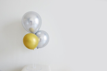Silver and gold balloons stand against white wall background
