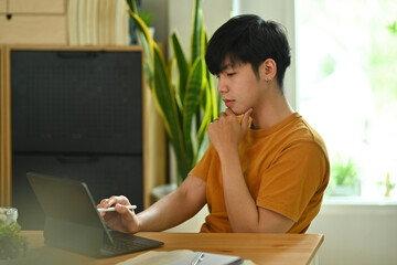 Photo of a young university student tutoring a lesson at the wooden table surrounded by a digital...
