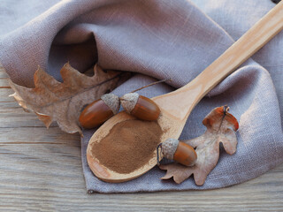 Ground acorn powder in wooden spoon, oak fruits, acorns and  autumn yellow leaves, napkin on a...