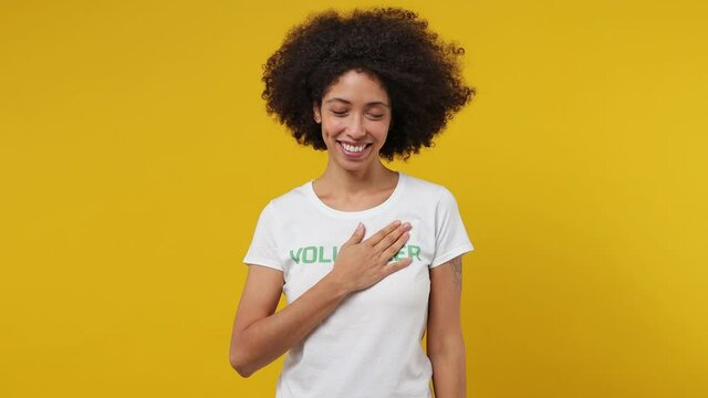 Young black woman 20s in white t-shirt green title volunteer showing shape heart with hands heart-shape sign isolated plain yellow background studio portrait. Voluntary free work help charity concept