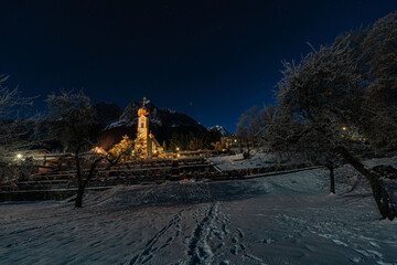 Kirche bei Nacht vor verschneiter Alpenlandschaft