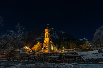 Kirche bei Nacht vor verschneiter Alpenlandschaft