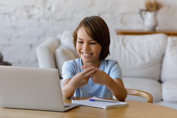 Happy teenage child boy looking at computer screen, making gestures, using sign language communicating online by video call with professional speech therapist, learning remotely alone at home.