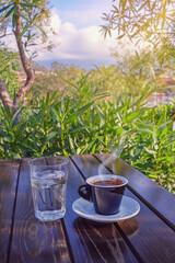 Morning coffee. Glass of water and  cup of coffee on table in garden