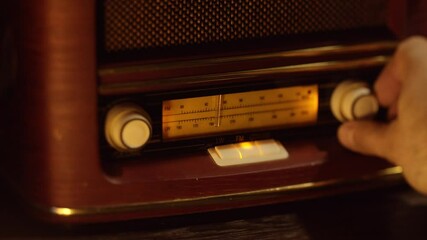 Vintage wooden retro radio receiver, macro shot of manual tuning of radio waves, hand turns the tuning knob. Slow camera movement from left to right.