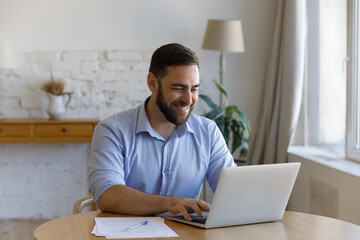 Smiling joyful millennial generation businessman entrepreneur manager enjoying working on computer,...