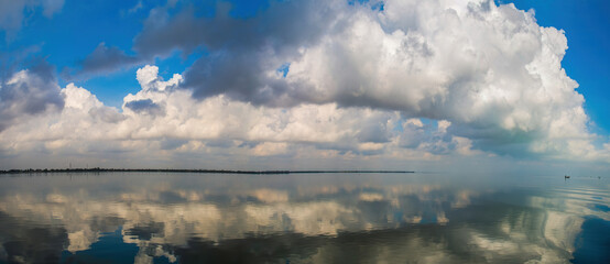 Panorama of a blue sky with clouds and water reflection 