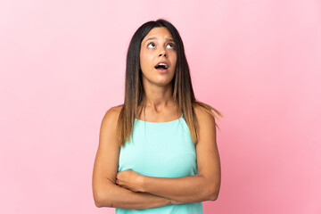 Caucasian girl isolated on pink background looking up and with surprised expression