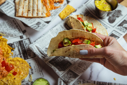 Female hands hold Mexican beef tacos with vegetables on restaurant table. Top view