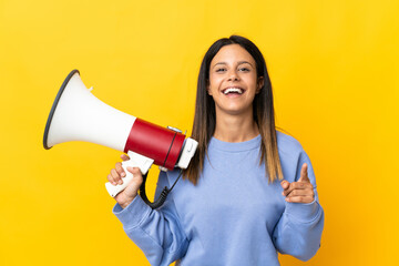 Caucasian girl isolated on yellow background holding a megaphone and smiling while pointing to the front