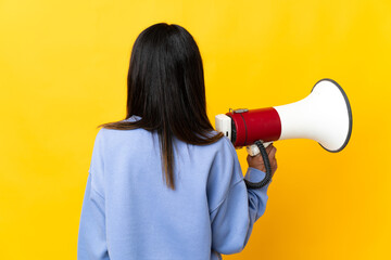 Caucasian girl isolated on yellow background holding a megaphone and in back position