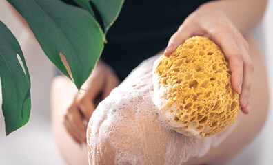 Young woman washing legs with yellow sponge and soap foam.