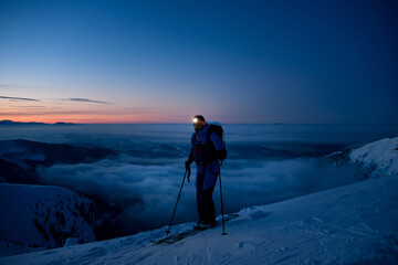 Fototapeta na wymiar male tourist skier with a flashlight on his forehead against the backdrop of picturesque evening sky