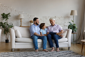 Happy bonding young daddy, small teenage kid son and middle aged old grandfather resting on...