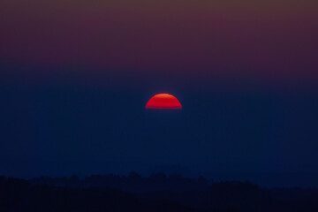 dramatic sky as the sun sets through low cloud with a glowing red golden silhouette, Wiltshire UK