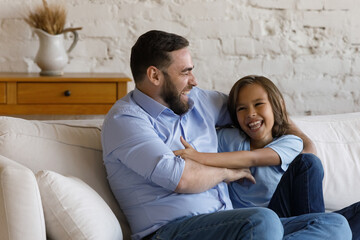 Happy friendly 35s father tickling laughing little teenage child son, spending time resting on cozy...
