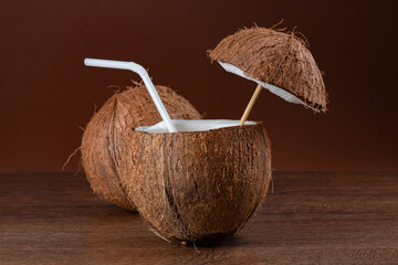 Coconut cocktail with a straw on brown background.
