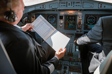Aircraft pilot studying documents before the flight in cockpit - obrazy, fototapety, plakaty
