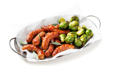 Appetizing sausages wrapped in bacon, garnished with brussel sprout and sage leaves. Holiday food. Isolated on white  background. 