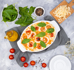 casserole, tomatoes, spinach leaves and seasonings on the table