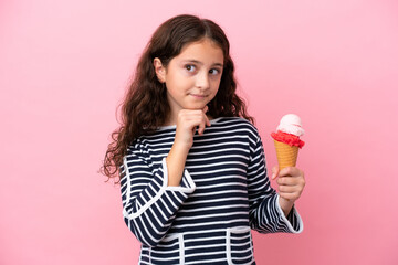 Little caucasian girl holding an ice cream isolated on pink background having doubts and thinking
