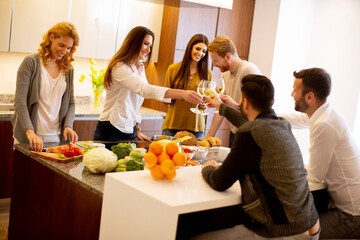 Group of young people preparing meal, drinking white wine and having a good time