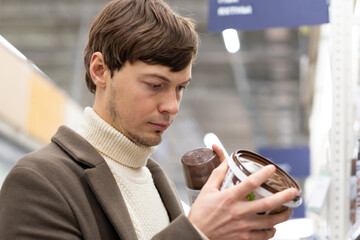 Short-haired brunet man with bristle wearing sweater and coat chooses paint for apartment...