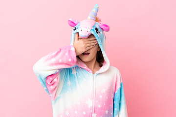 Little caucasian woman wearing a unicorn pajama isolated on pink background covering eyes by hands. Do not want to see something © luismolinero