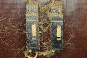 two old black plastic toggle switches on an electric meter in gray dust and cobwebs on a brown wall