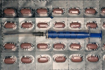 a blue syringe with a needle lies on gray packs of brown pills
