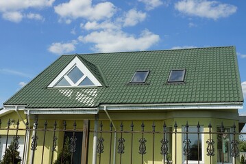 a yellow private house under a green tiled roof with windows behind a black iron fence with sharp...