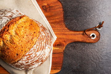 Wholemeal sourdough bread on linen napkin on brown wooden chopping board.