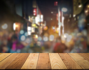 Empty wooden table top with blur image of city night market outdoor with burry people and light bokeh in a perspective background, copy space for your text ready for product promotion display montage