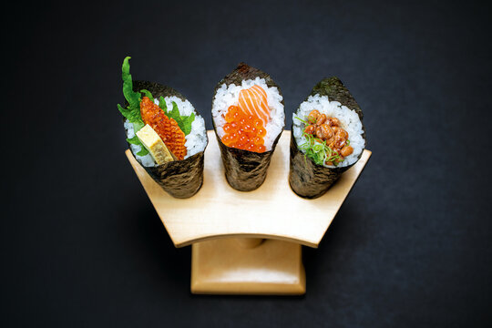 Set of temaki sushi from smoked eel, omelette, shiso, salmon, caviar, natto, negi in wooden hand roll stand on black background. Traditional Japanese cuisine.