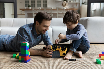 Little son repairing toy car with loving young father, using screwdriver, sitting playing on warm...