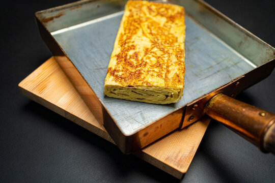 Dashimaki a Japanese style rolled omelet. Egg Sushi Marinated with Dashi Soup, Mirin and Shoyu. In a Tamagoyaki copper pan on a wooden serving board. 