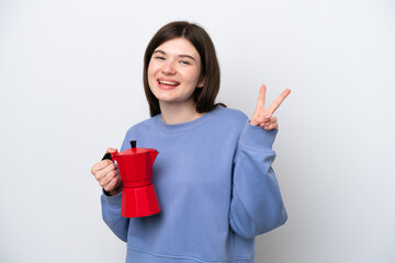 Young Russian woman holding coffee pot isolated on white background smiling and showing victory sign