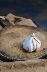 
White garlic on a brown wooden chopping board with a beige napkin and two broken slices.