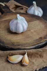 White garlic on a brown wooden chopping board with a beige napkin and two broken slices.