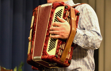 Detail of a man in a white checkered shirt playing the red accordion