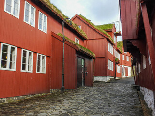 Eine Strasse führt hinauf durch die Altstadt von Torshavn, vorbei an mehreren roten Holzhäusern 