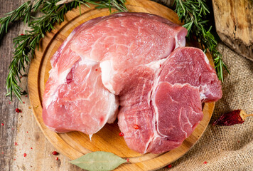 A large piece of raw pork with rosemary lies on a board on a wooden table. The view is over. Flat lay.
